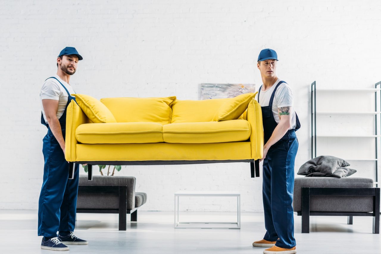 two movers in uniform transporting couch in apartment
